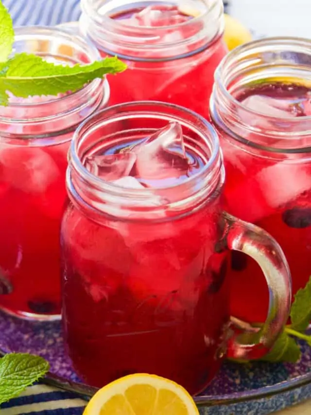 Mason jar handled glasses with blueberry lemonade garnished with blueberries, mint, and lemons halves.