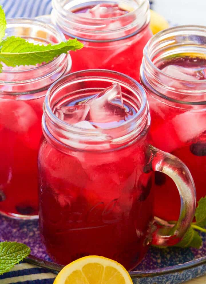 Mason jar handled glasses with blueberry lemonade garnished with blueberries, mint, and lemons halves.