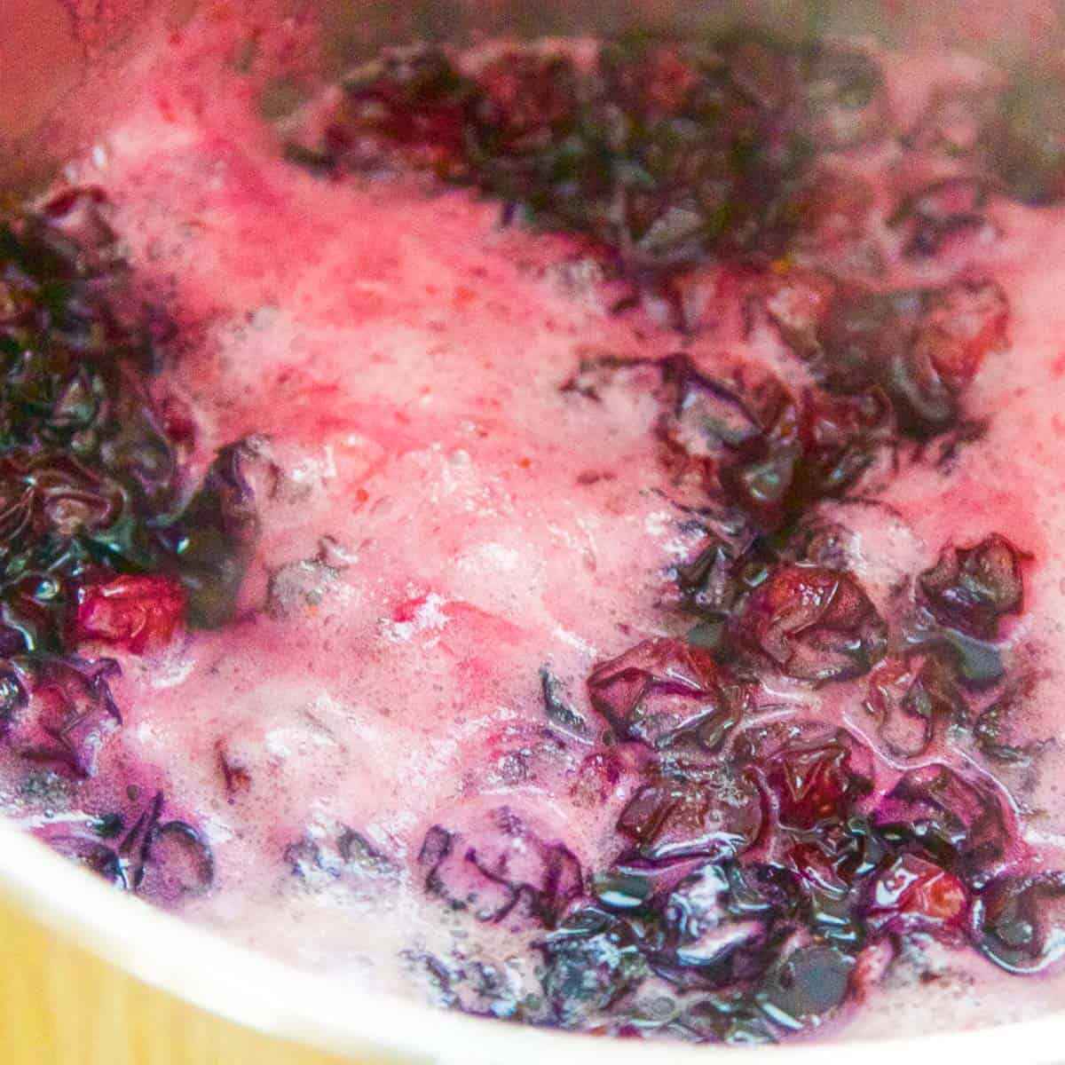 Making blueberry syrup with the sugar and blueberries bubbling in a pot.