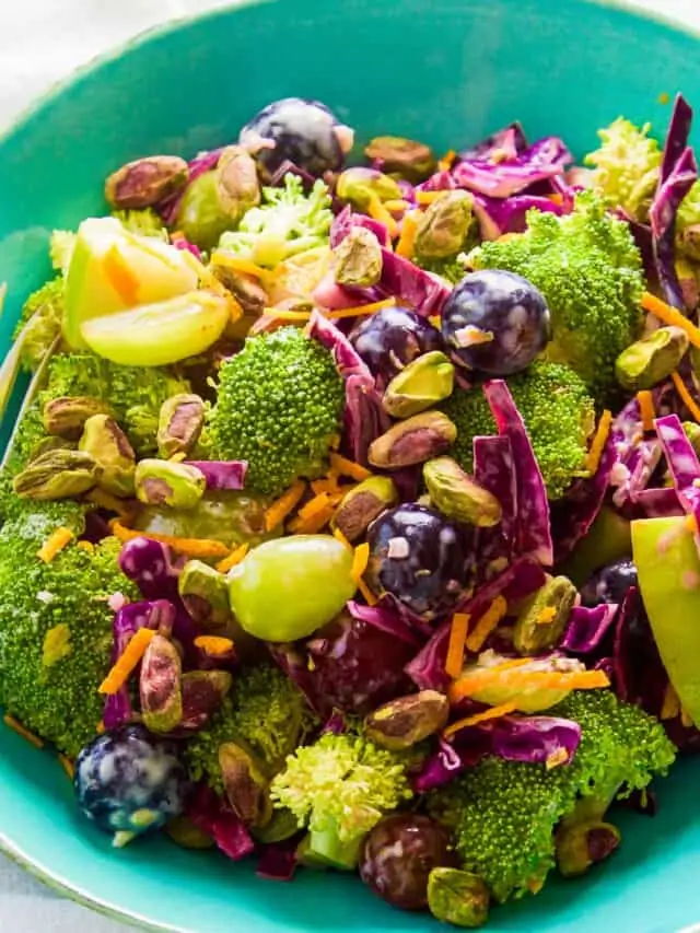A turquoise salad bowl filled with broccoli salad with colorful grapes and pistachios.