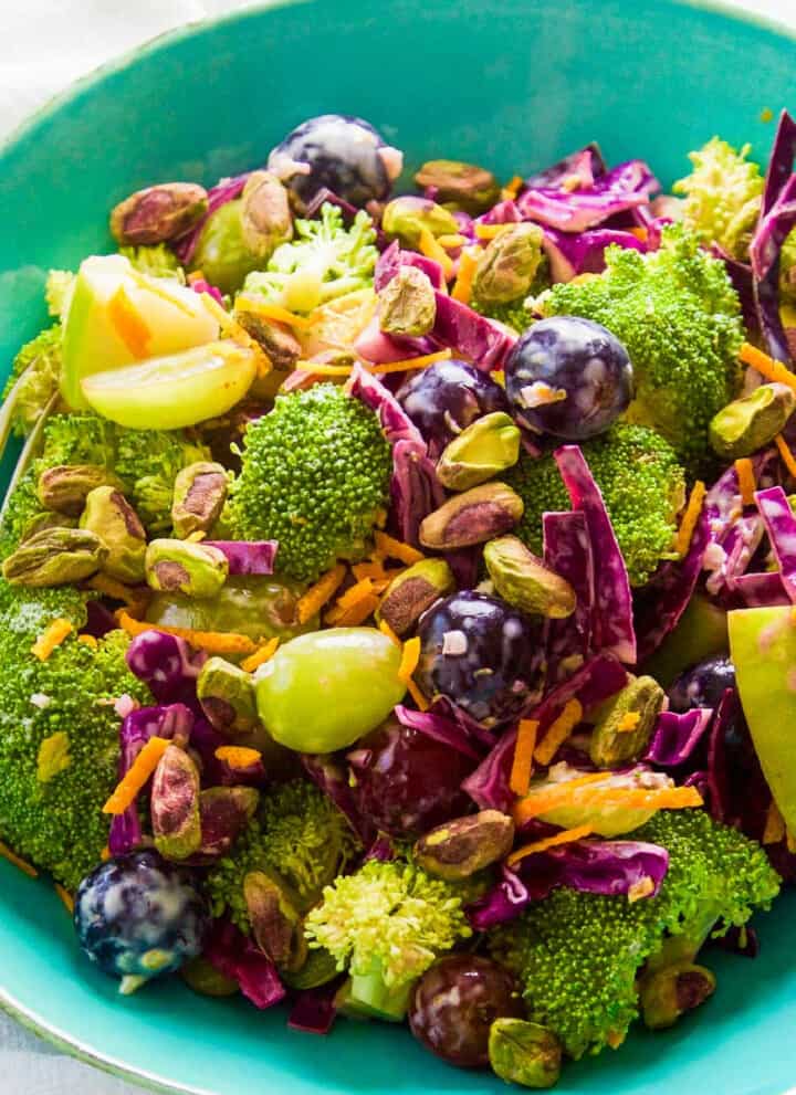 A turquoise salad bowl filled with broccoli salad with colorful grapes and pistachios.