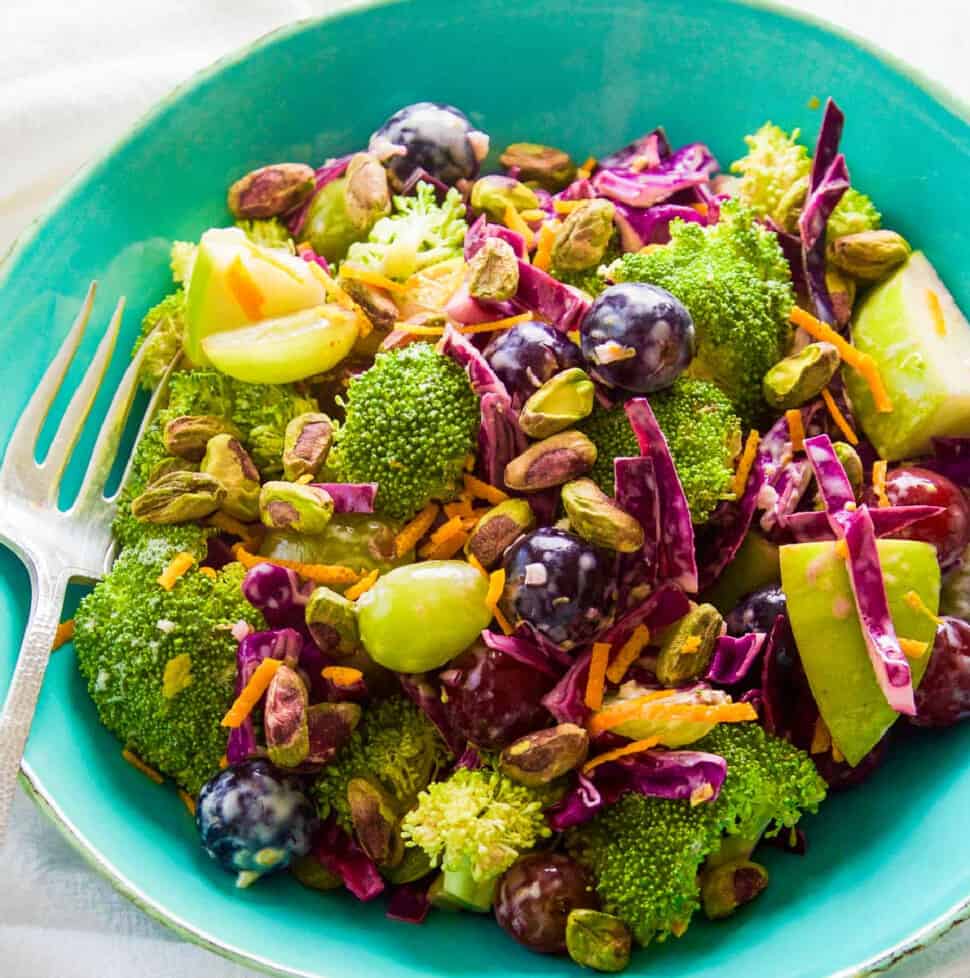 A turquoise salad bowl filled with broccoli salad with colorful grapes and pistachios.