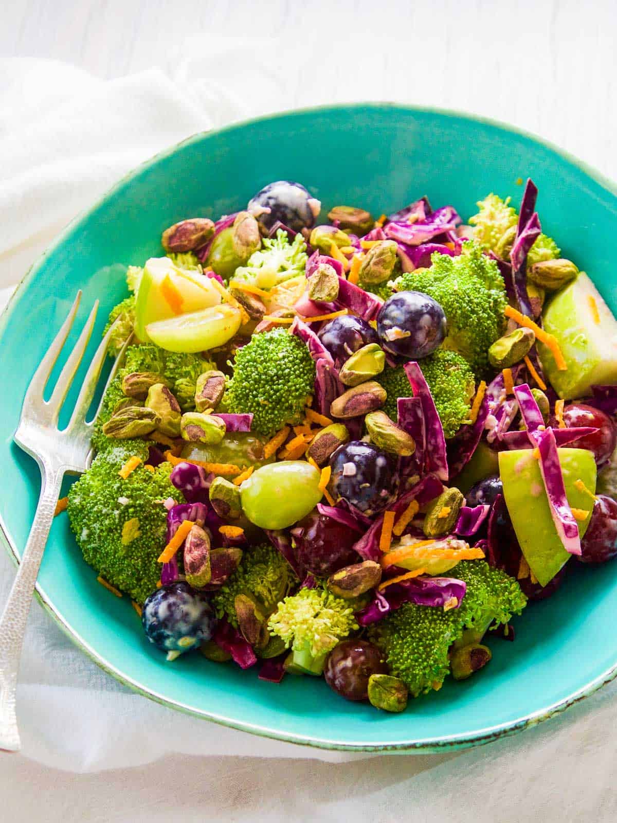 A turquoise blue bowl filled with colorful broccoli salad with pistachios and grapes.