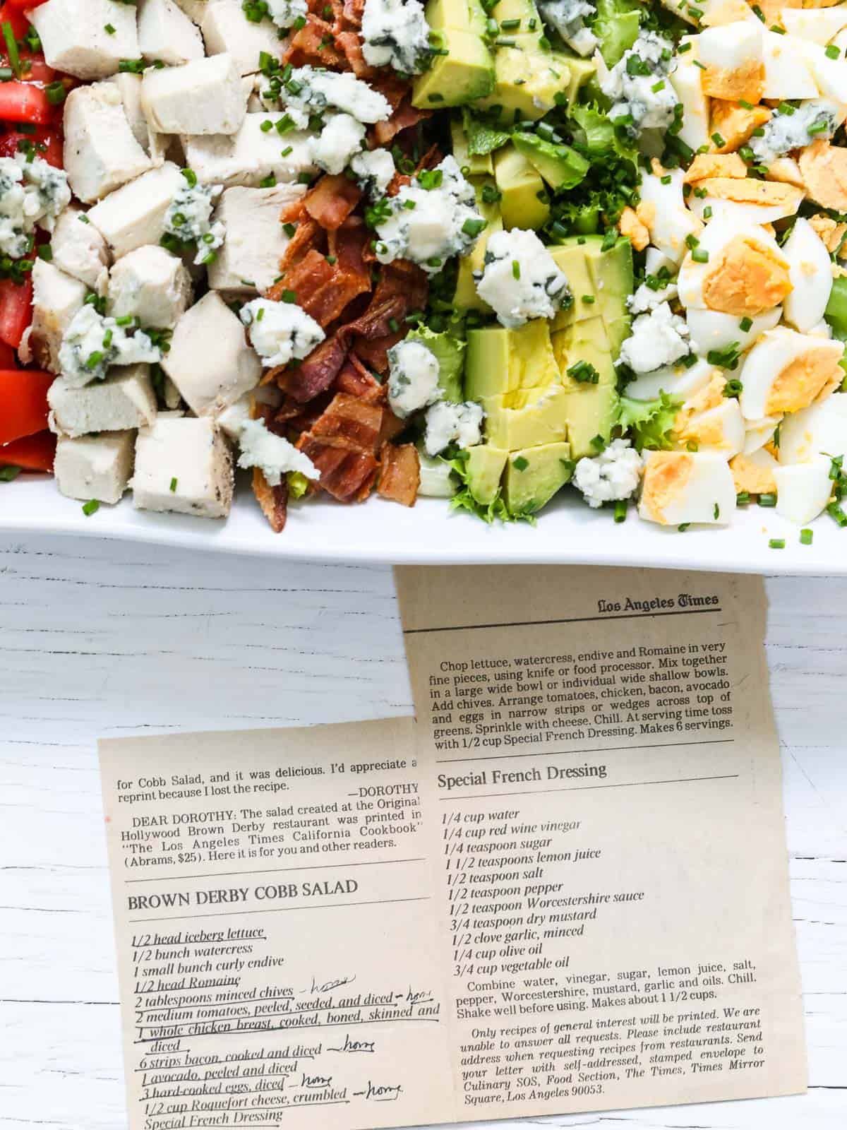 Edge of white square plate with Cobb Salad and the original recipe printed in LA Times.