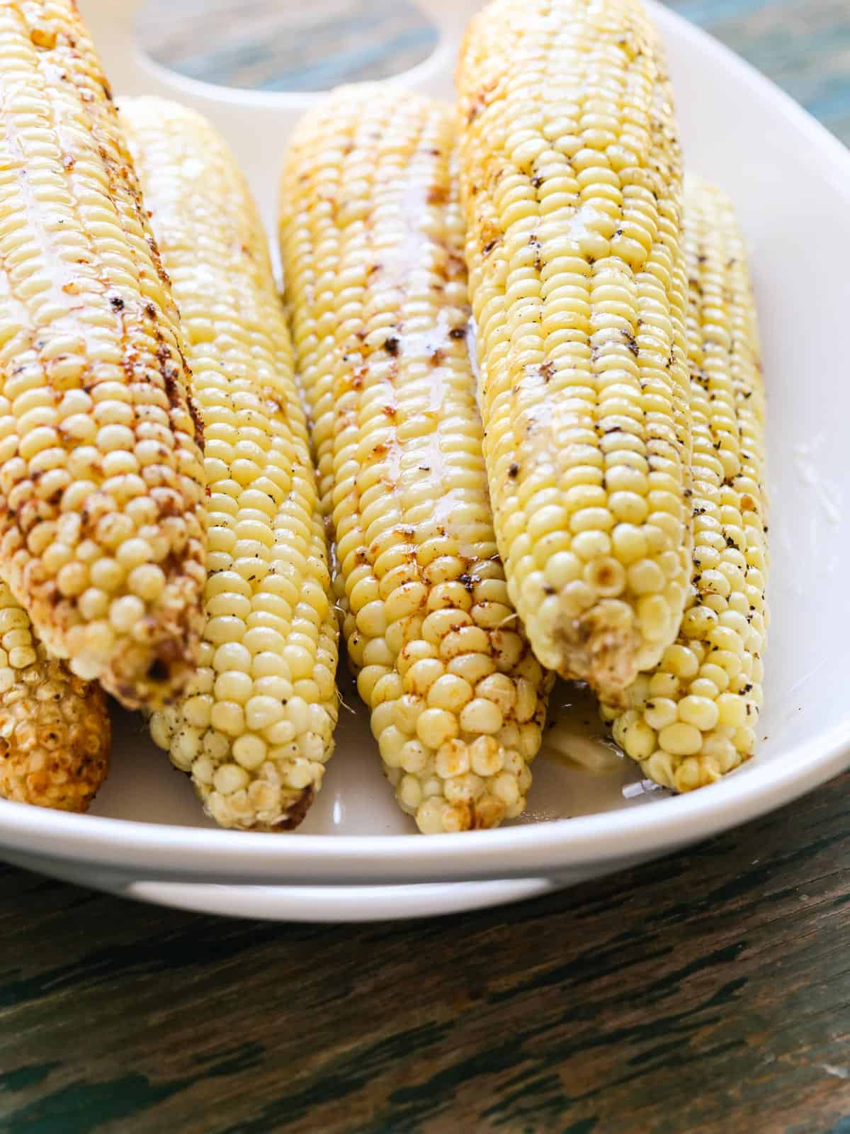 A white oval platter with grilled corn and melted butter on top.