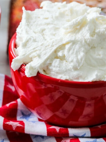 A red bowl with fluffy vanilla frosting ready to frost a cake.