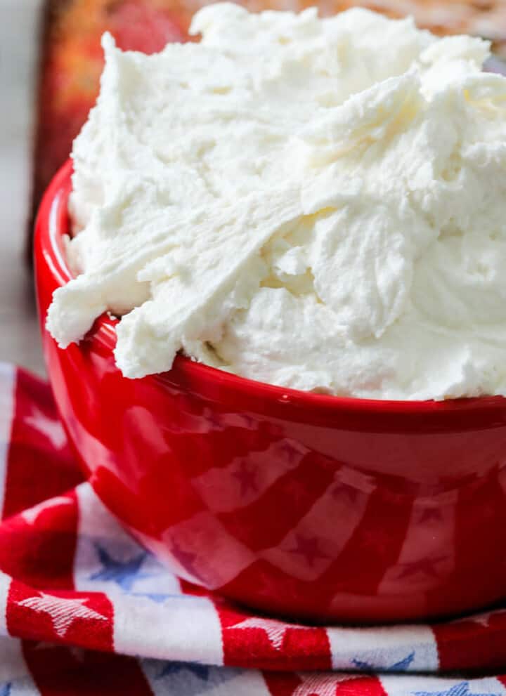 A red bowl with fluffy vanilla frosting ready to frost a cake.