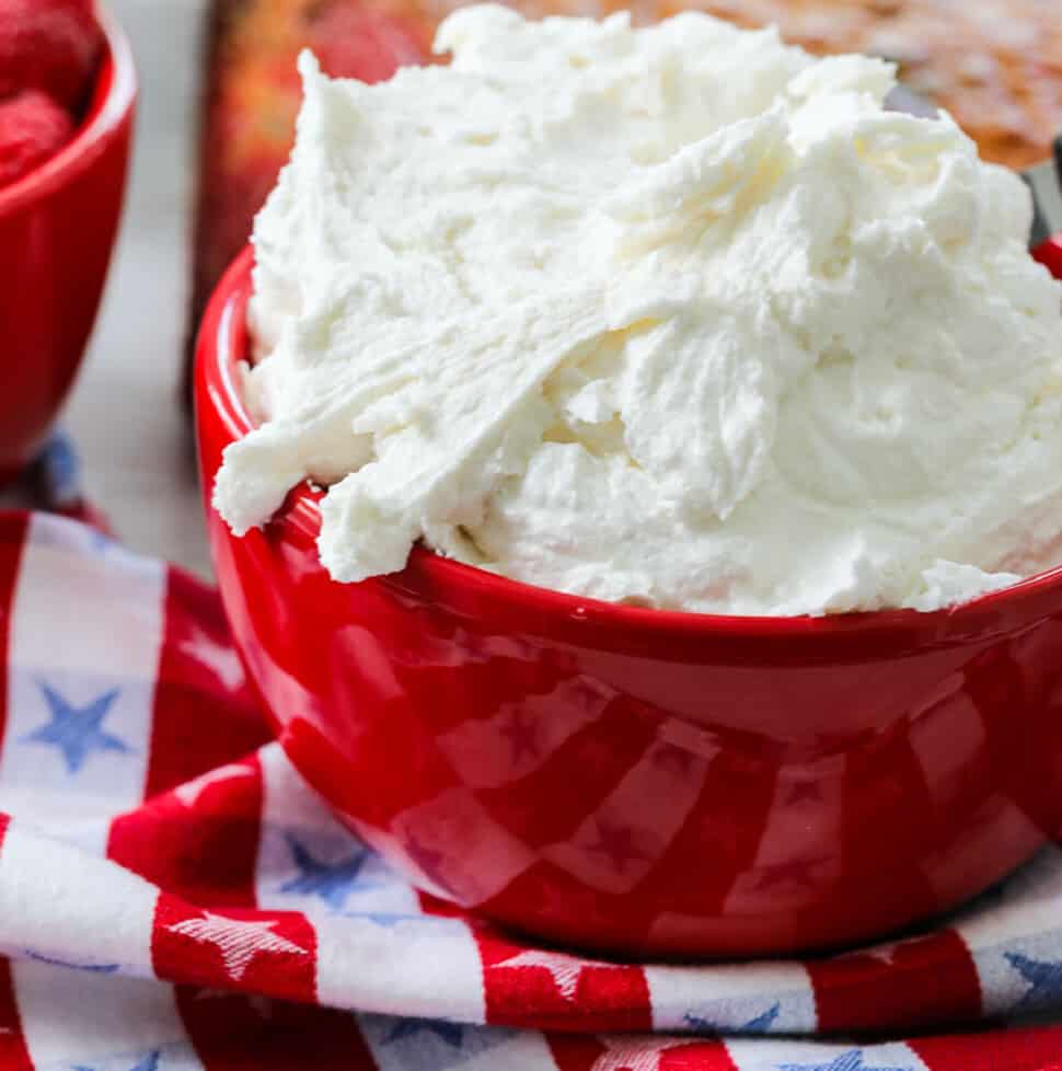 A red bowl with fluffy vanilla frosting ready to frost a cake.