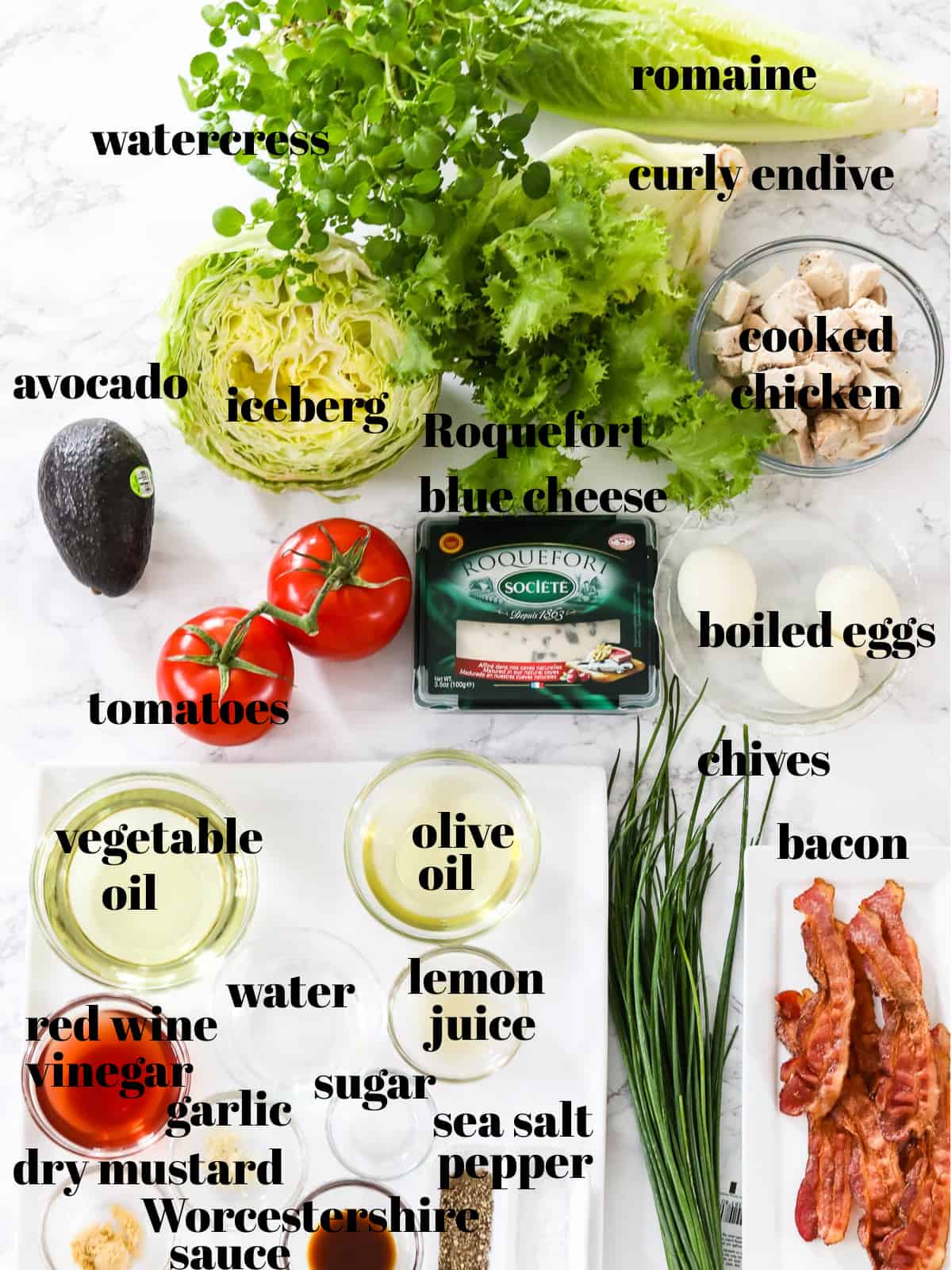 All the ingredients on a table listed to make Cobb Salad including lettuce, bacon and blue cheese.