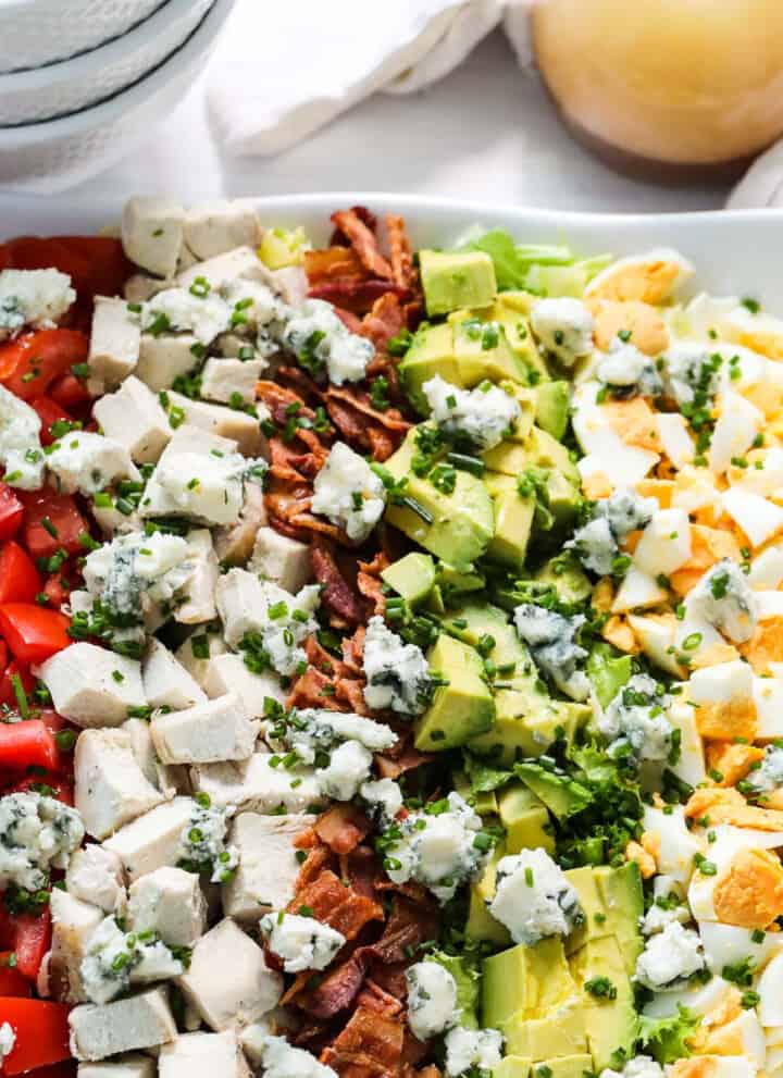 A white square plate filled with colorful Cobb Salad made with chicken, eggs, avocados, tomatoes, and bacon.