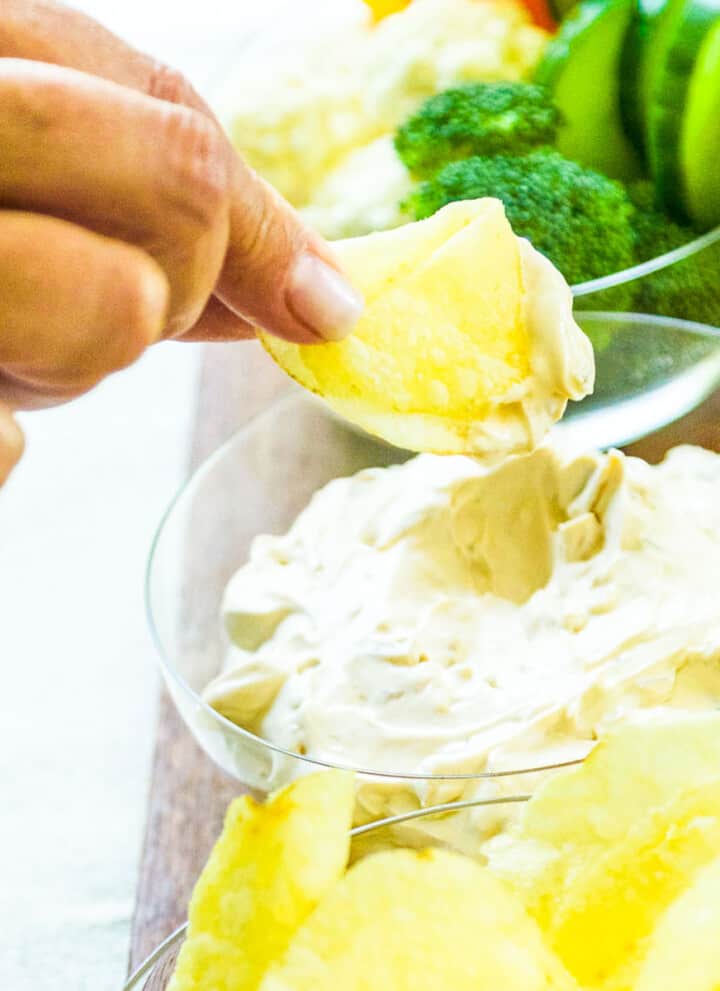 A lady dipping a potato chip into onion dip.