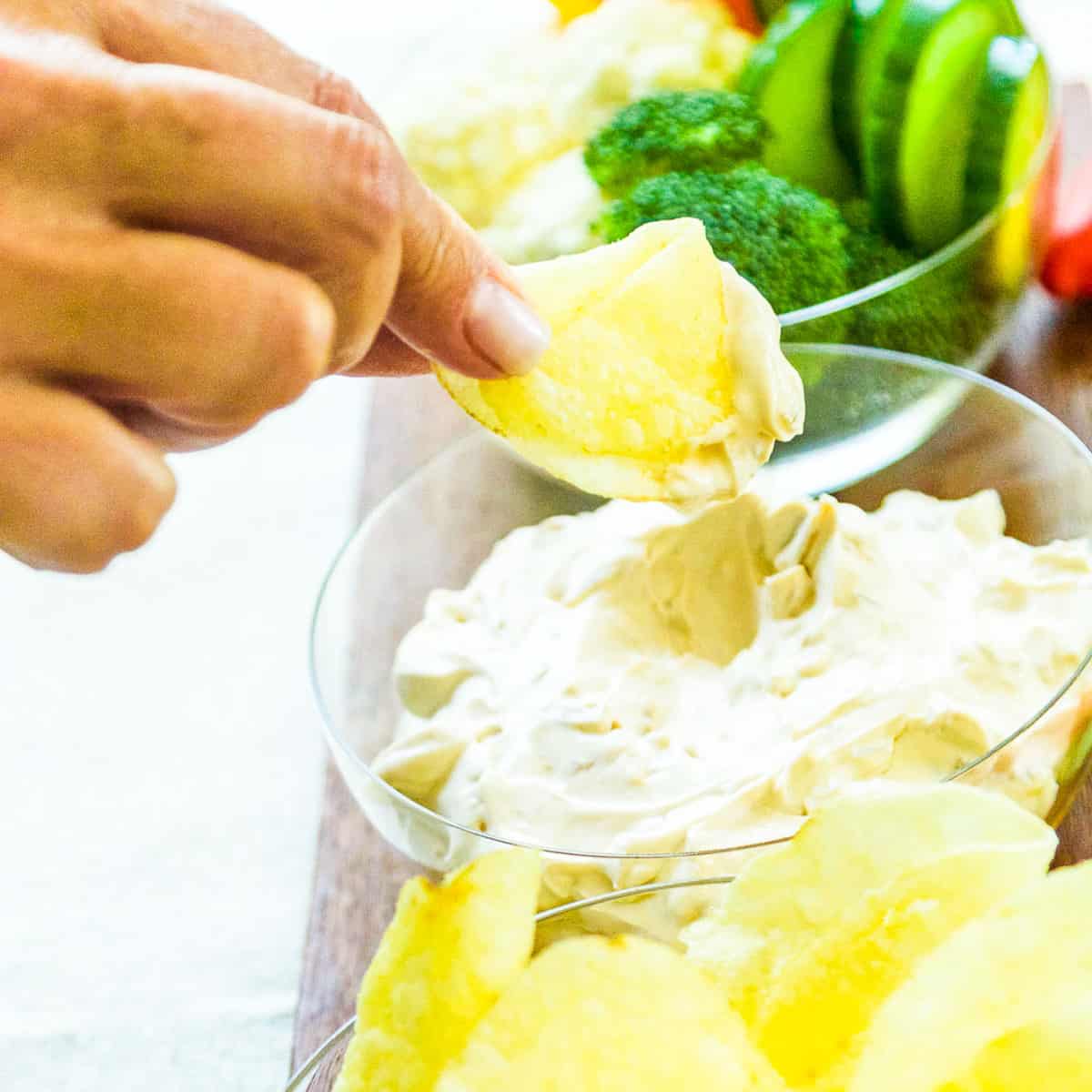 A lady dipping a potato chip into onion dip.