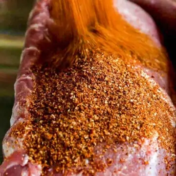 A large pork loin roast with a lot of dry rub seasoning pouring over the top.