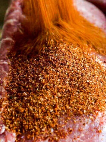 A large pork loin roast with a lot of dry rub seasoning pouring over the top.