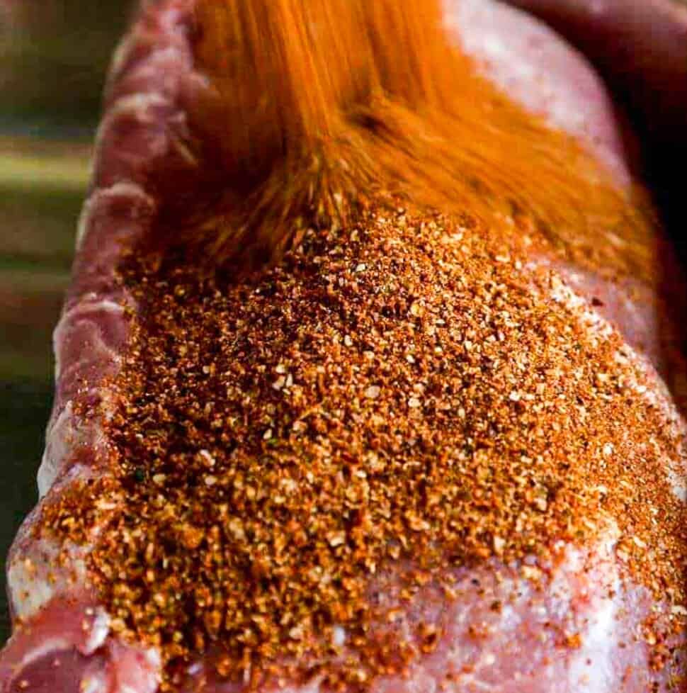 A large pork loin roast with a lot of dry rub seasoning pouring over the top.