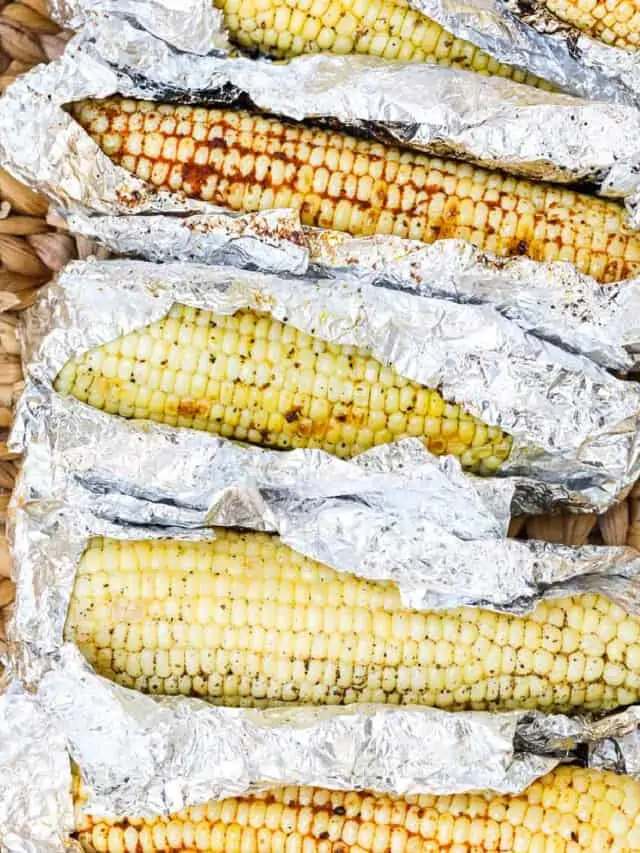 A larger serving basket with Grilled Corn unwrapped in foil laying in the basket before eating.