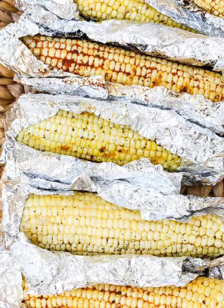 A larger serving basket with Grilled Corn unwrapped in foil laying in the basket before eating.