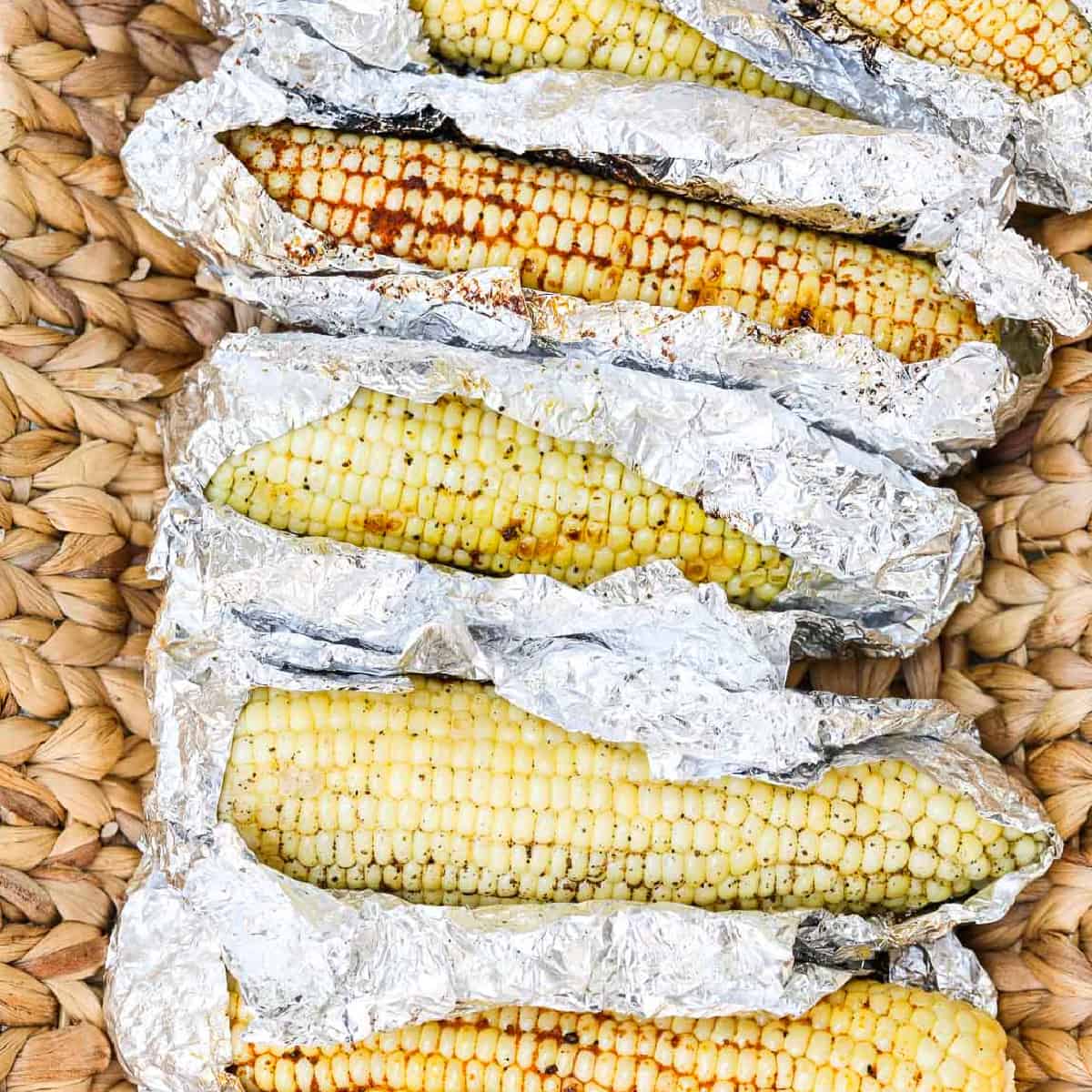 A larger serving basket with Grilled Corn unwrapped in foil laying in the basket before eating.