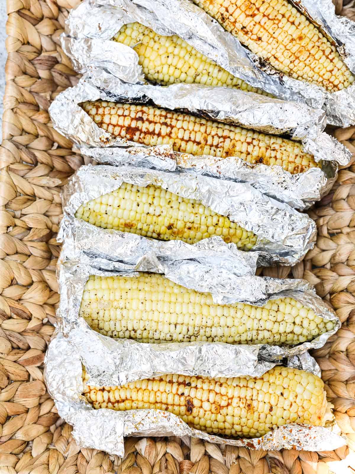 A larger serving basket with Grilled Corn unwrapped in foil laying in the basket before eating.