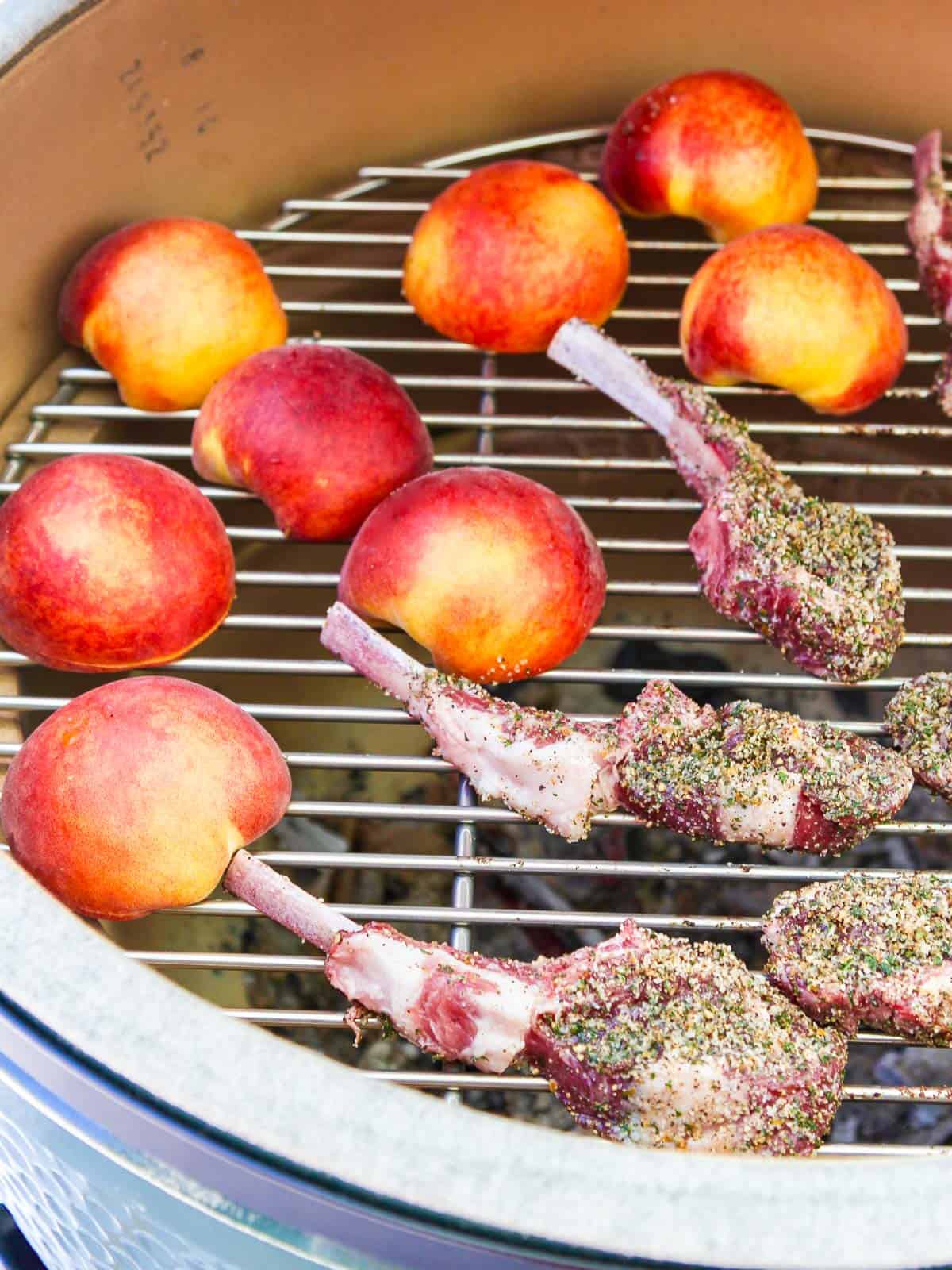 A charcoal grill with lamb chops and peaches grilling over hot coals. 