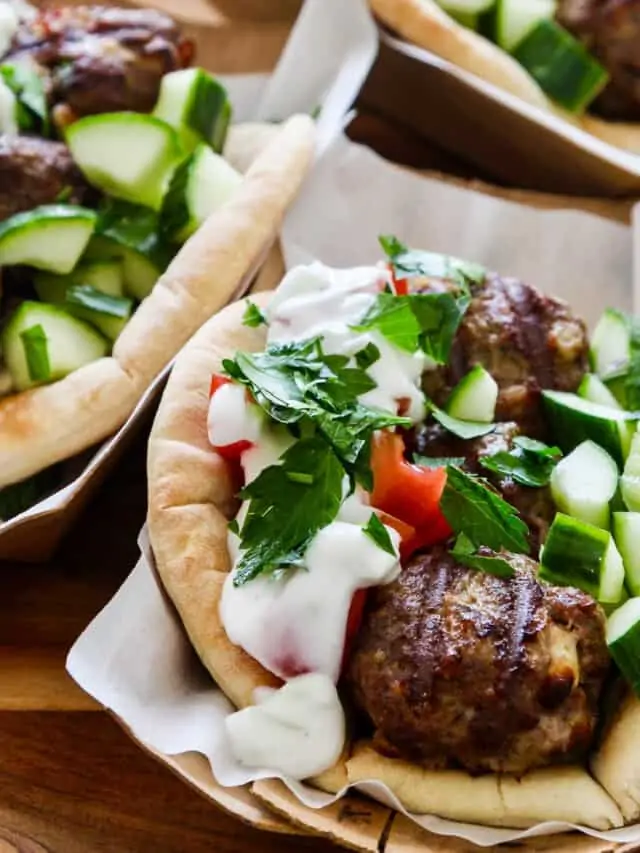 Greek gyros on parchment paper topped with lamb meatballs cucumber and tomatoes.