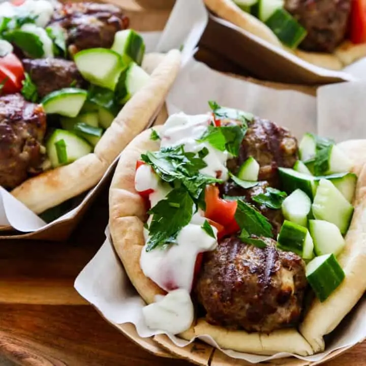 Greek gyros on parchment paper topped with lamb meatballs cucumber and tomatoes.