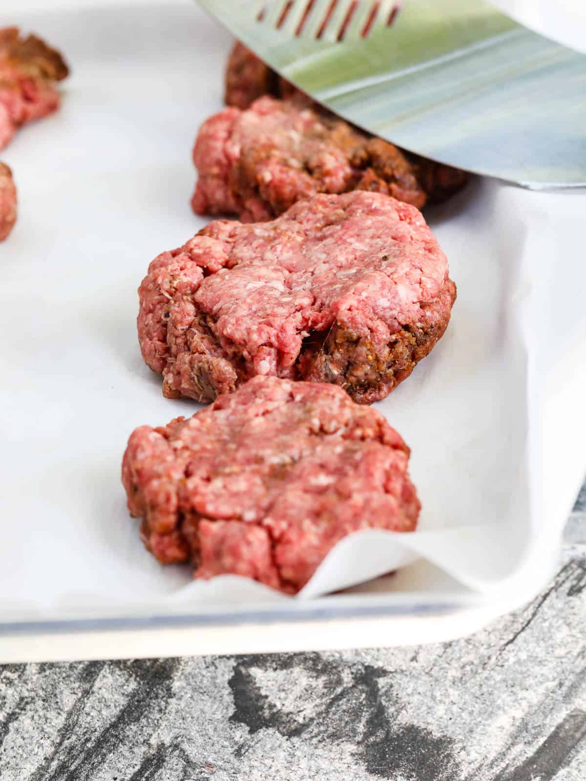 A parchment lined sheet pan with hamburger patties ready to grill.