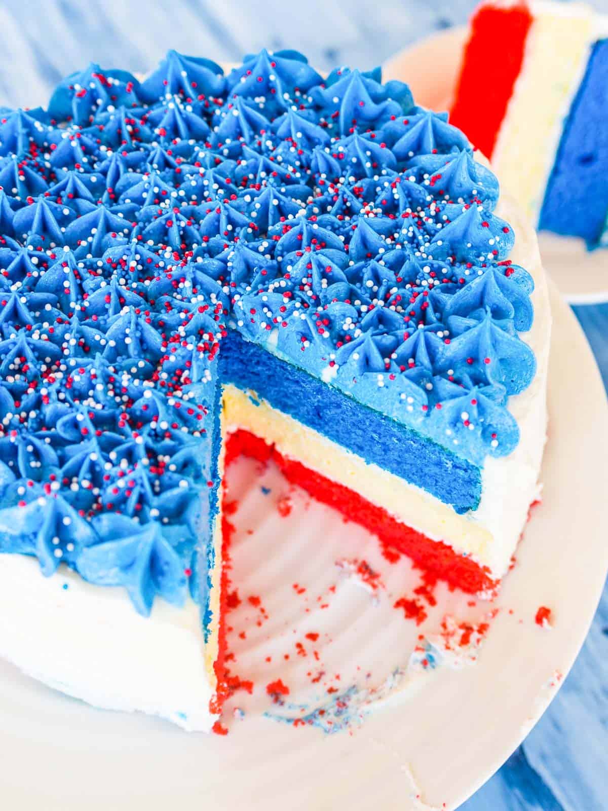 A beautful layered cake with red white and blue layers, and blue star tip icing and sprinkles for July 4th.
