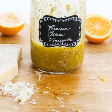 A mason jar with lemon vinaigrette inside on a messy cutting board.