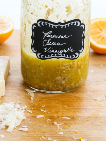 A mason jar with lemon vinaigrette inside on a messy cutting board.