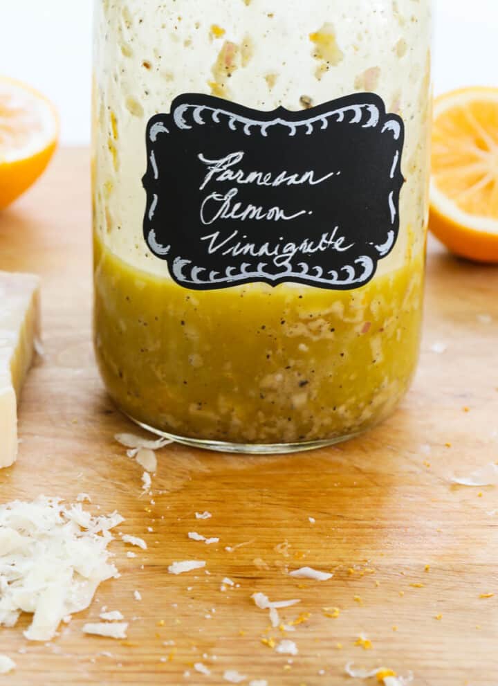 A mason jar with lemon vinaigrette inside on a messy cutting board.