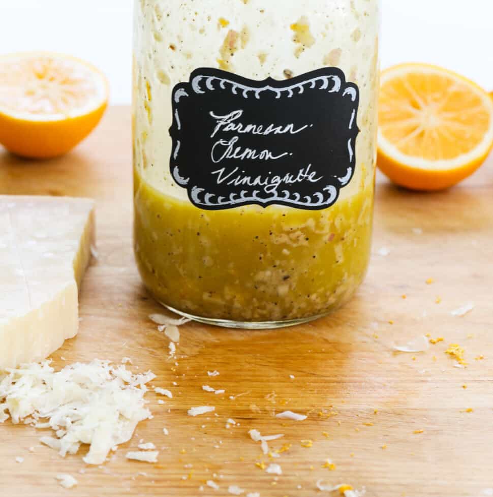 A mason jar with lemon vinaigrette inside on a messy cutting board.