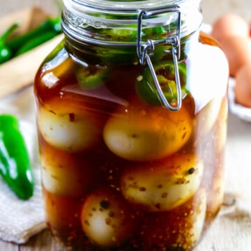 A large glass clamp jar filled with pickled eggs, fresh jalapeno slices, and spices.