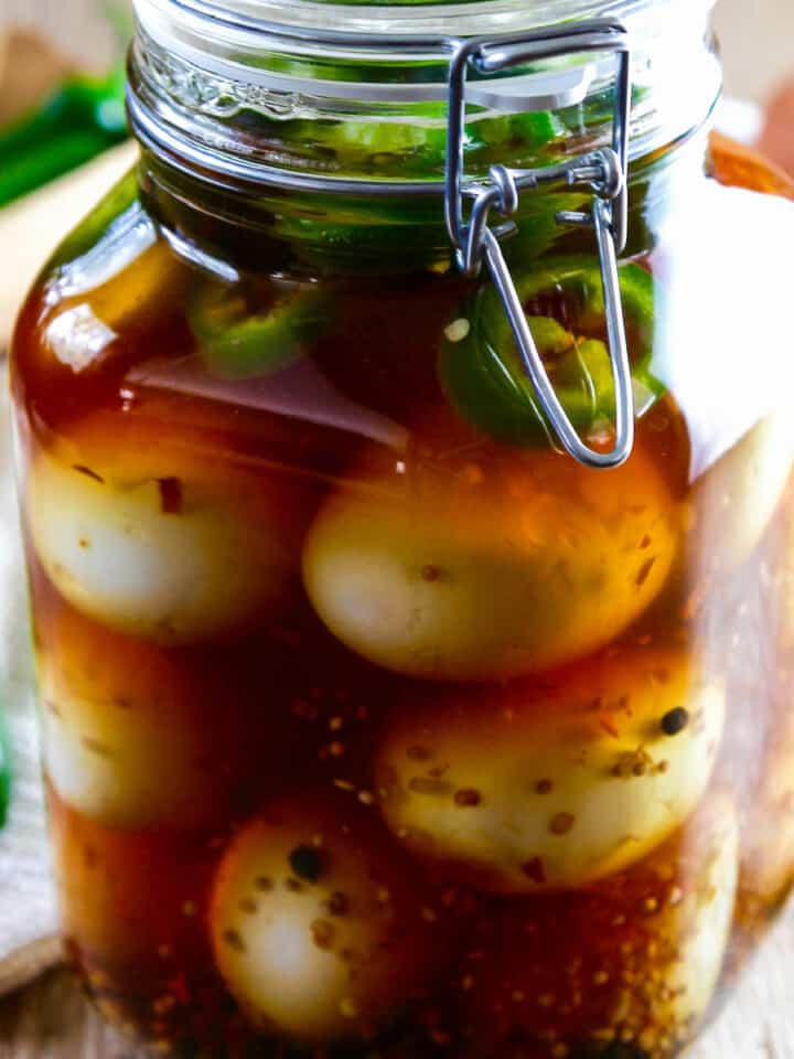 A large glass clamp jar filled with pickled eggs, fresh jalapeno slices, and spices.