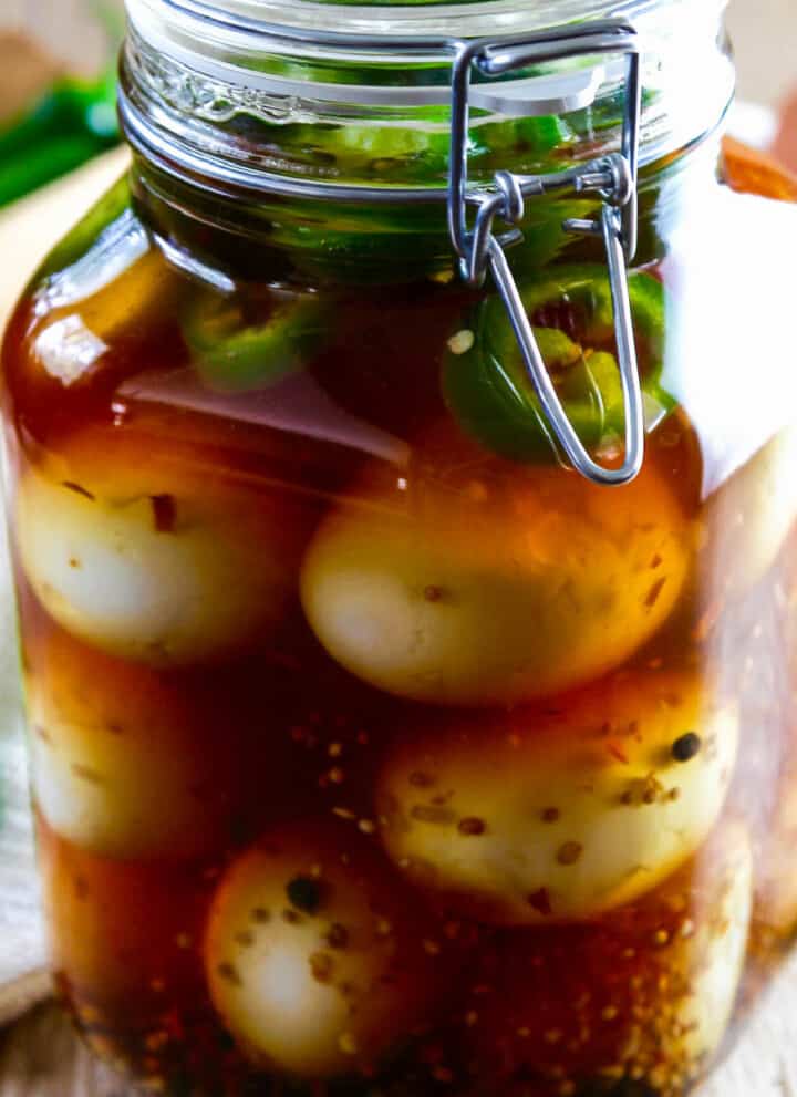 A large glass clamp jar filled with pickled eggs, fresh jalapeno slices, and spices.