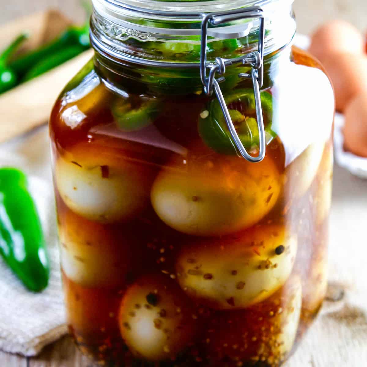 A large glass clamp jar filled with pickled eggs, fresh jalapeno slices, and spices.