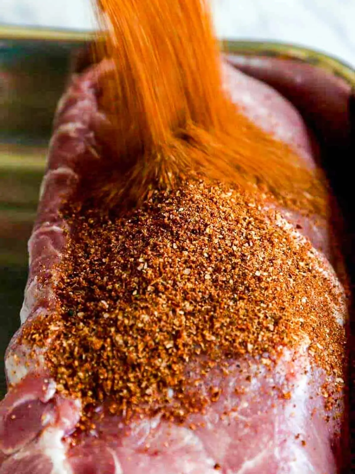 A large pork loin roast with a lot of dry rub seasoning pouring over the top.