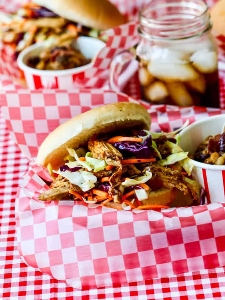 Red white check paper lined basked holding a pulled pork sandwich topped with coleslaw.