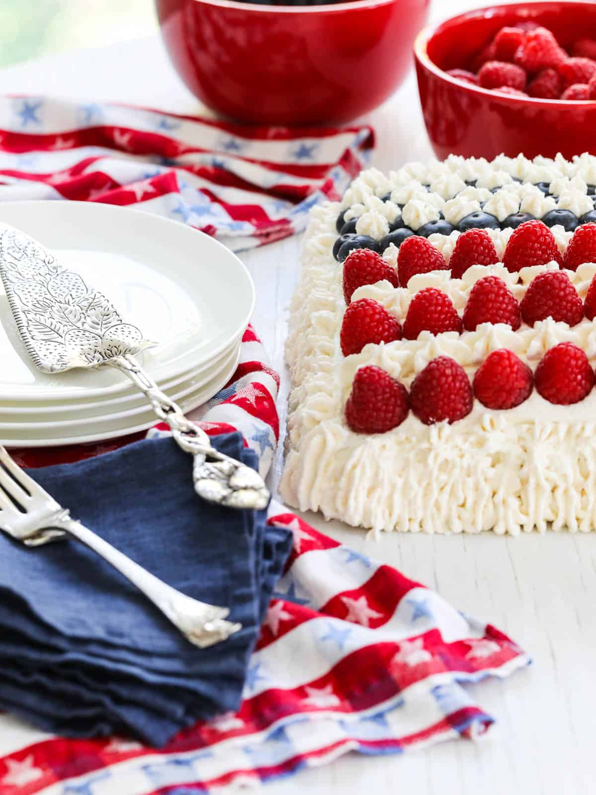 Close up of the corner on a Flag Cake decorated with white frosting, raspberries, and blueberries.