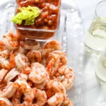 A clear glass plate with shrimp cocktail, cocktail sauce, and two glasses of champagne.