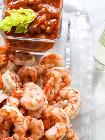 A clear glass plate with shrimp cocktail, cocktail sauce, and two glasses of champagne.