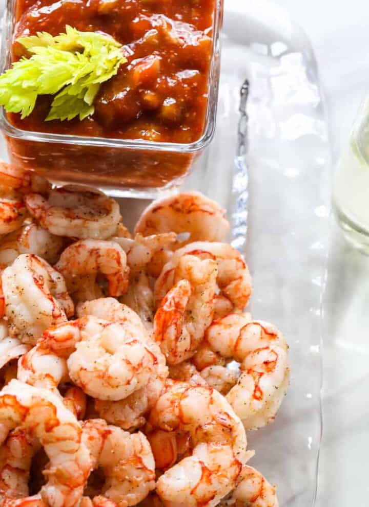 A clear glass plate with shrimp cocktail, cocktail sauce, and two glasses of champagne.