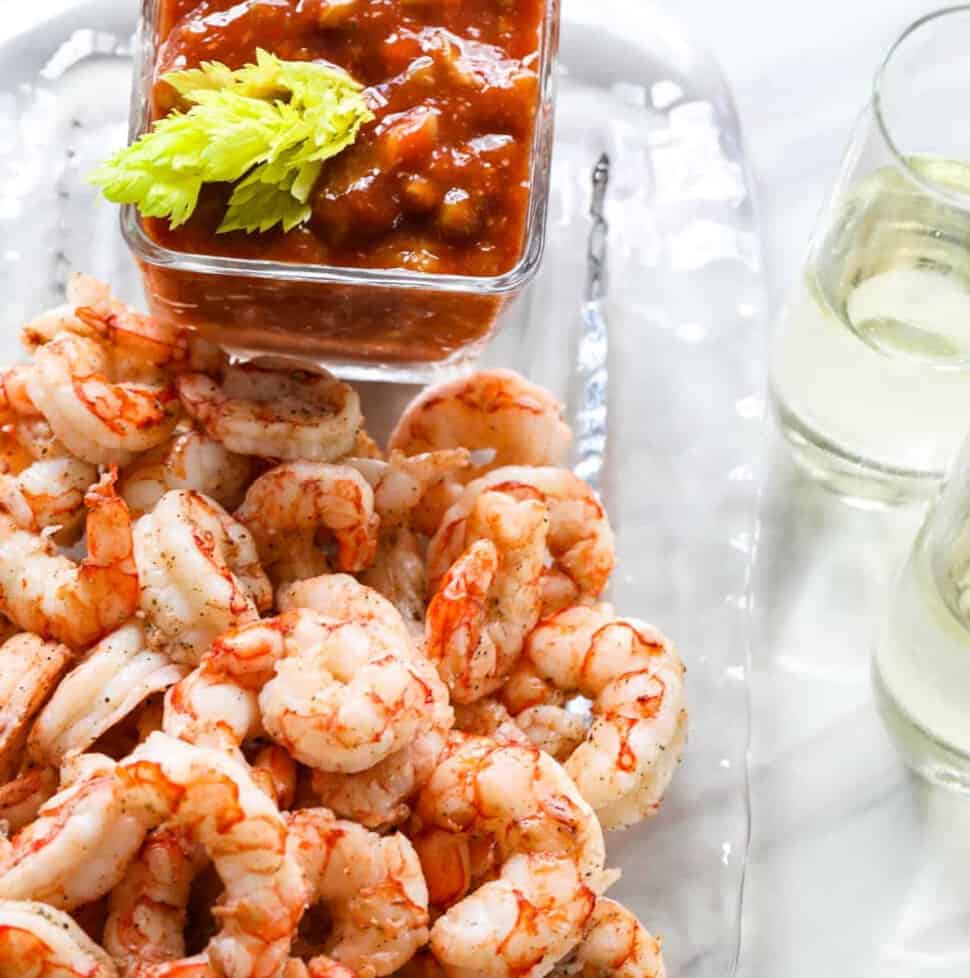 A clear glass plate with shrimp cocktail, cocktail sauce, and two glasses of champagne.