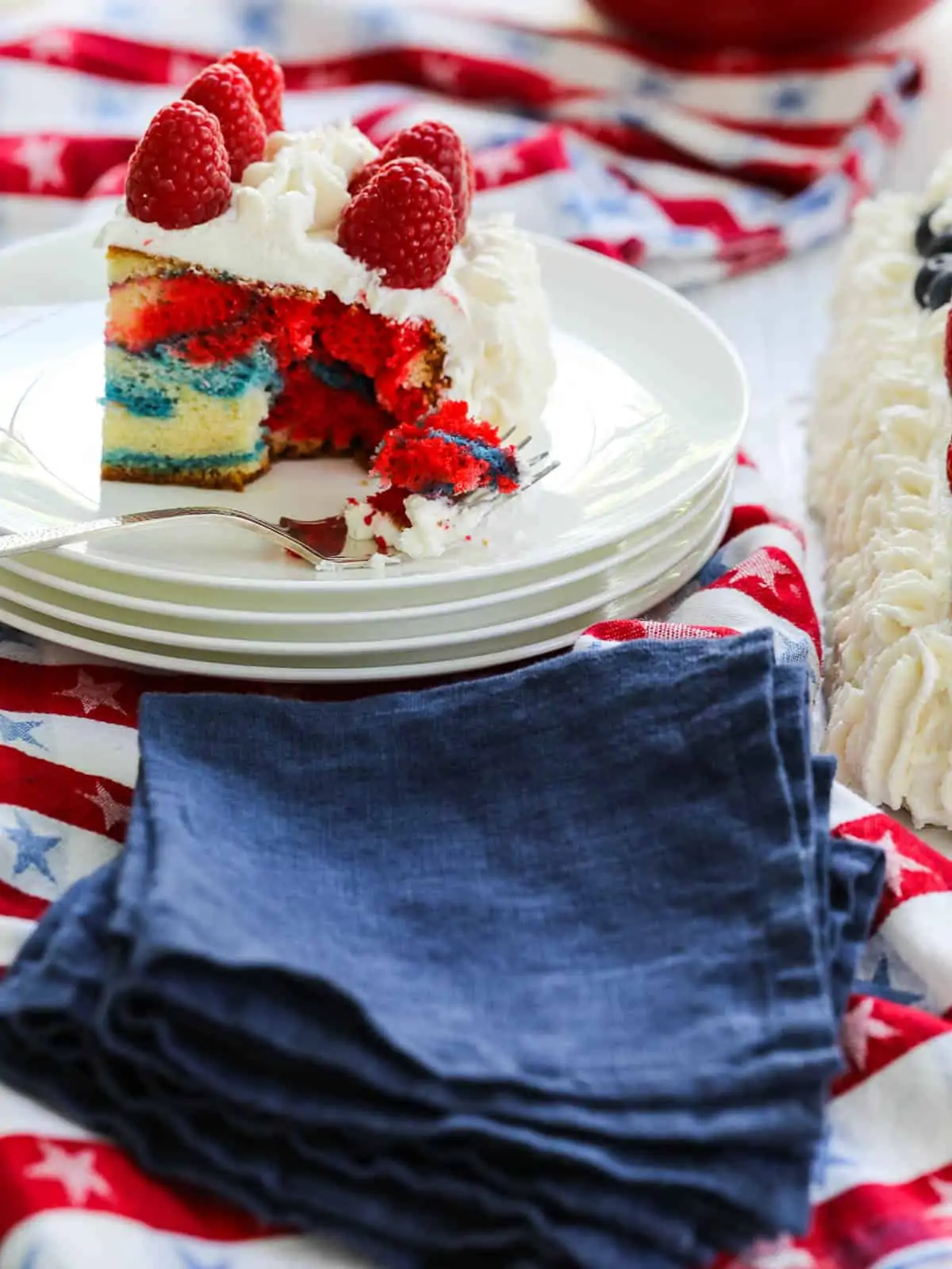 One slice of red white and blue marbled cake decorated with white frosting and raspberries.