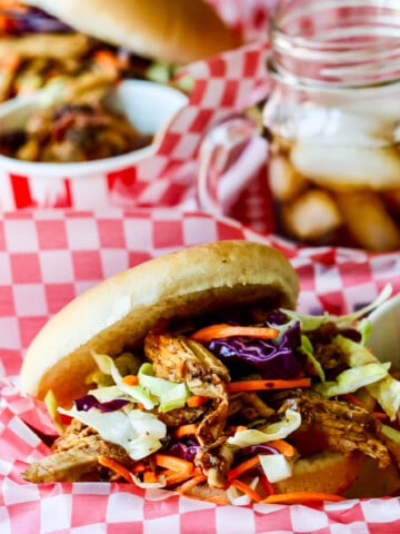 Red white check paper lined basked holding a pulled pork sandwich topped with coleslaw.