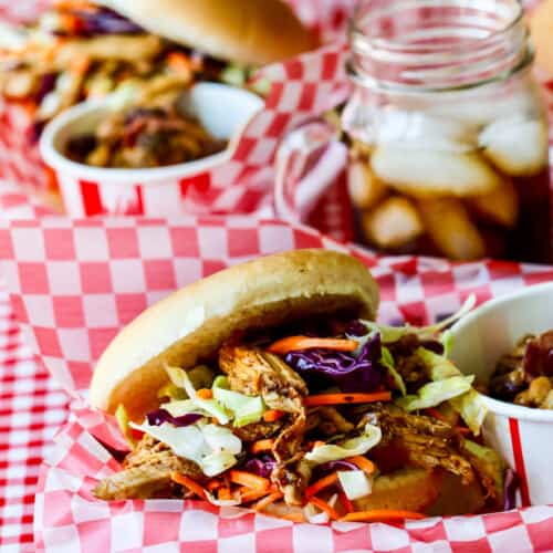 Red white check paper lined basked holding a pulled pork sandwich topped with coleslaw.