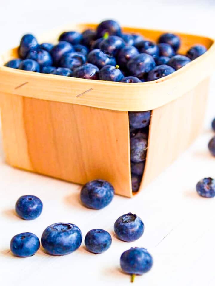 A wood box filled with fresh blueberries and some on a white table.