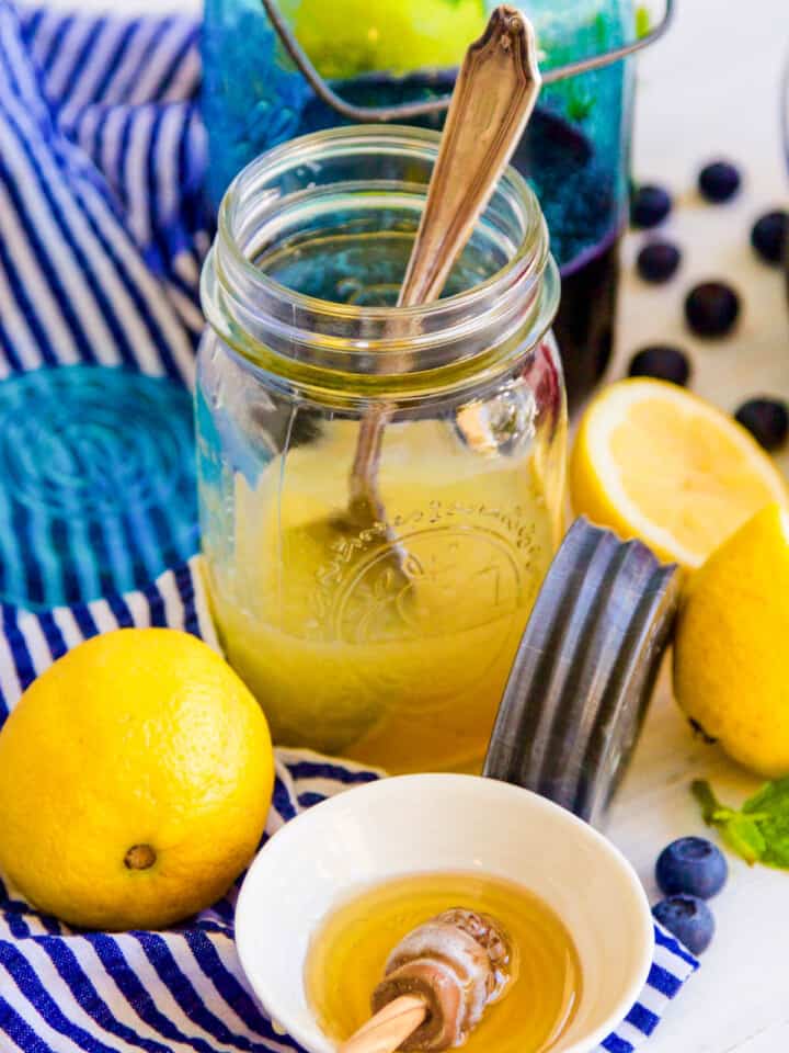 A large jar filled with fresh squeezed lemon juice with lemons nearby.