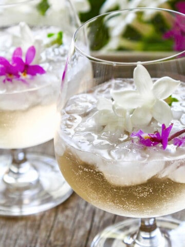 Two glasses filled with St Germain cocktails garnished with tiny purple orchids and white jasmine flowers.