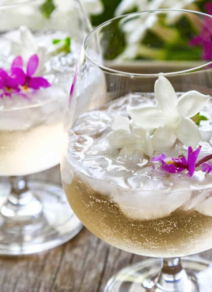 Two glasses filled with St Germain cocktails garnished with tiny purple orchids and white jasmine flowers.